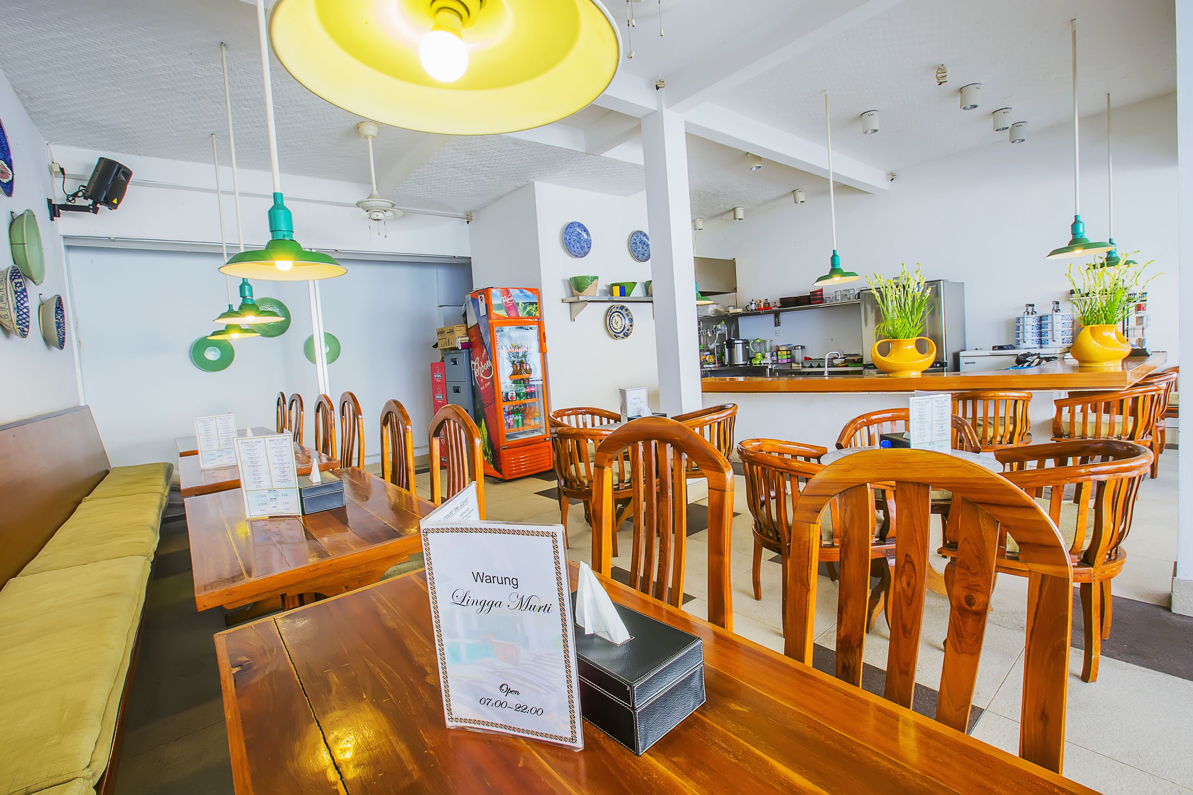 A restaurant interior with wooden tables and chairs, hanging green pendant lights, and a menu stand.