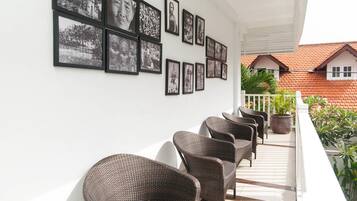 A balcony with wicker chairs and a row of black-and-white photographs on the wall.