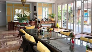 A spacious dining area with a long table, wicker chairs with yellow cushions, and a decorative ceiling. - Samsara Inn (Kuta)