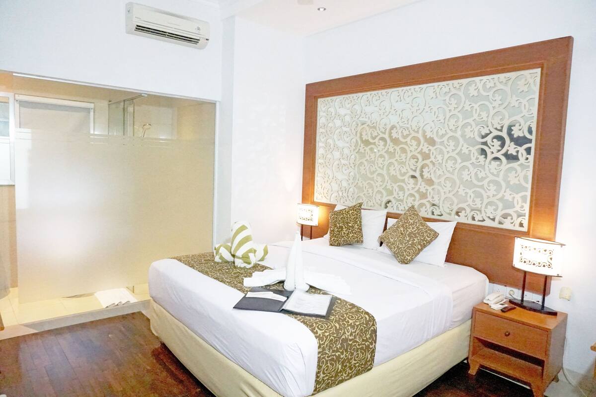 A hotel room with a large bed, a nightstand with a lamp, a decorative headboard, and a shower area.