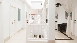 A bright, white hallway with a central white railing, a ceiling fan, and a view of a room with a chair and a desk. - Samsara Inn (Kuta)