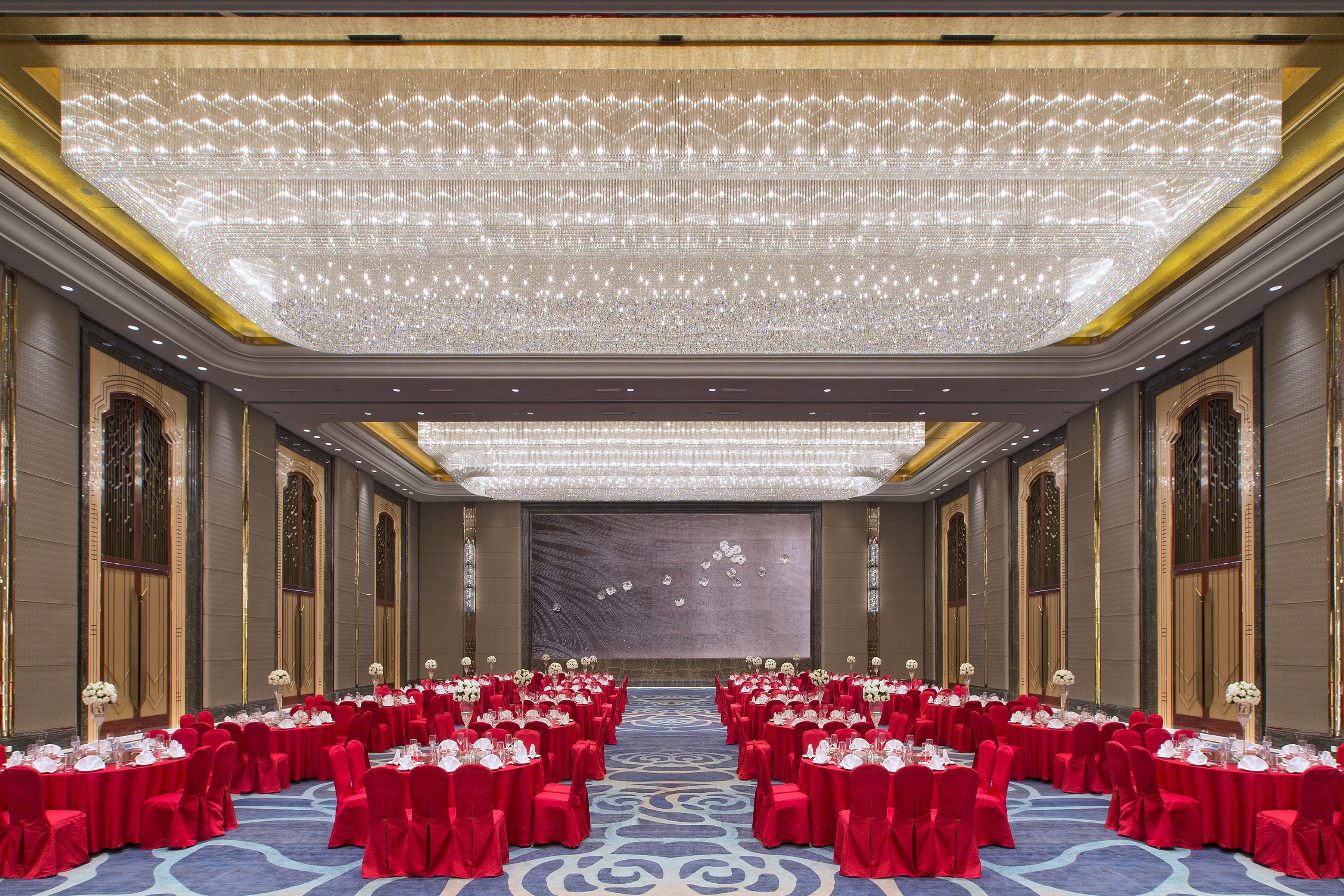 Een balzaal met rijen tafels gedekt voor een formeel evenement, met een grote kroonluchter en versierde wanddecoraties.