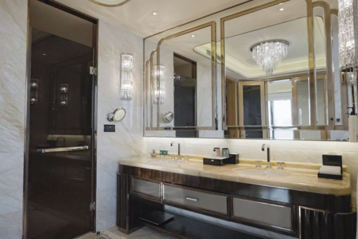 Un baño moderno con un espejo grande, un tocador con lavamanos y una araña.