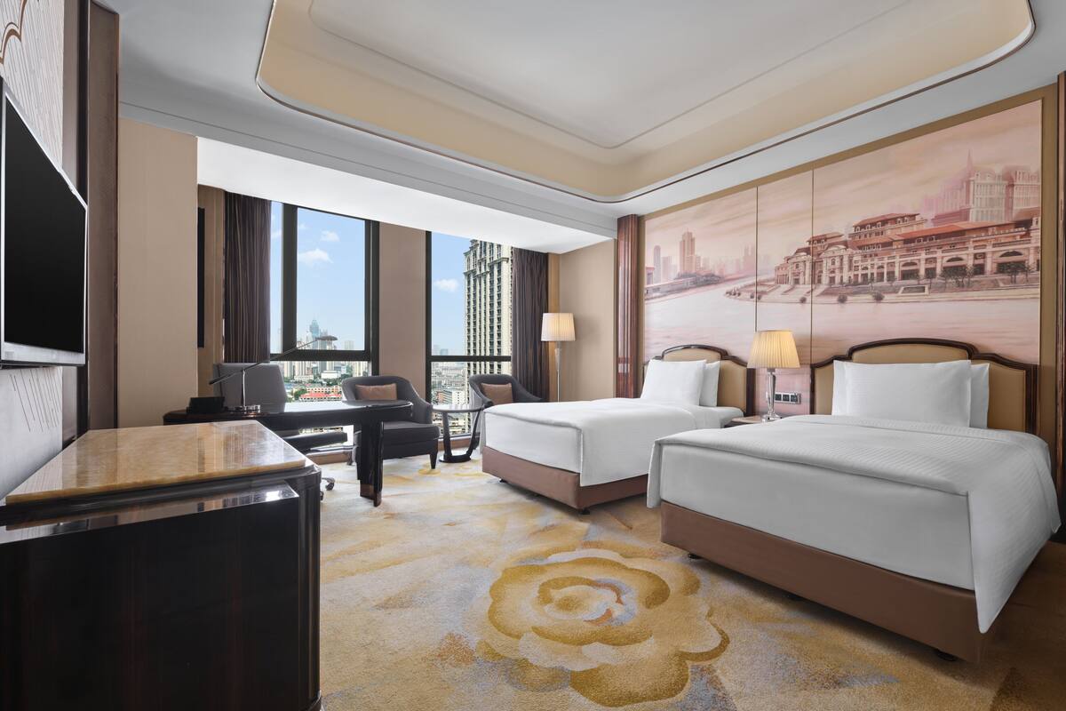 Une chambre d’hôtel avec deux lits, un bureau et une grande fenêtre donnant sur la ville.