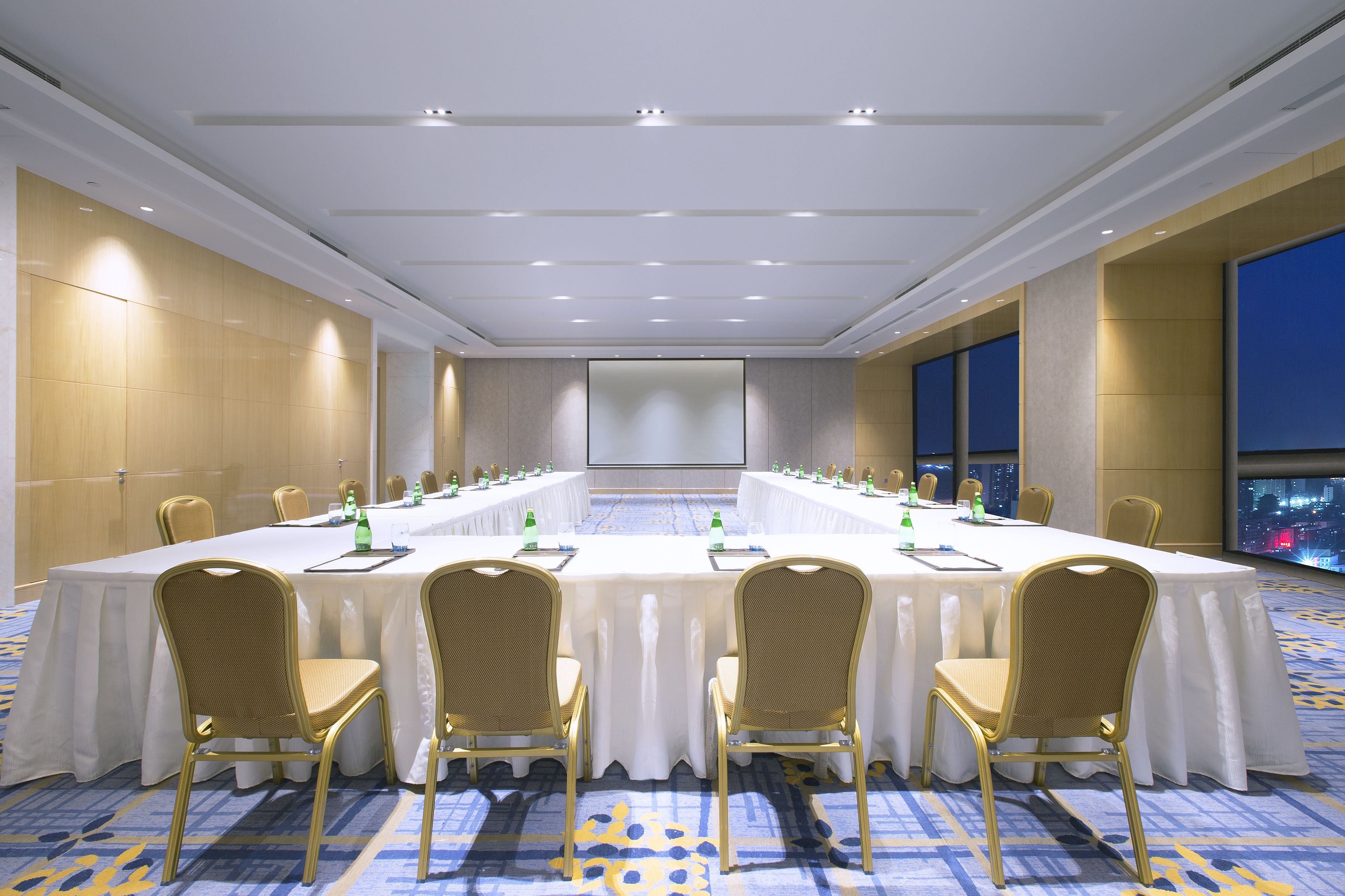 Un salón de conferencias con una larga mesa, sillas y una pantalla grande.