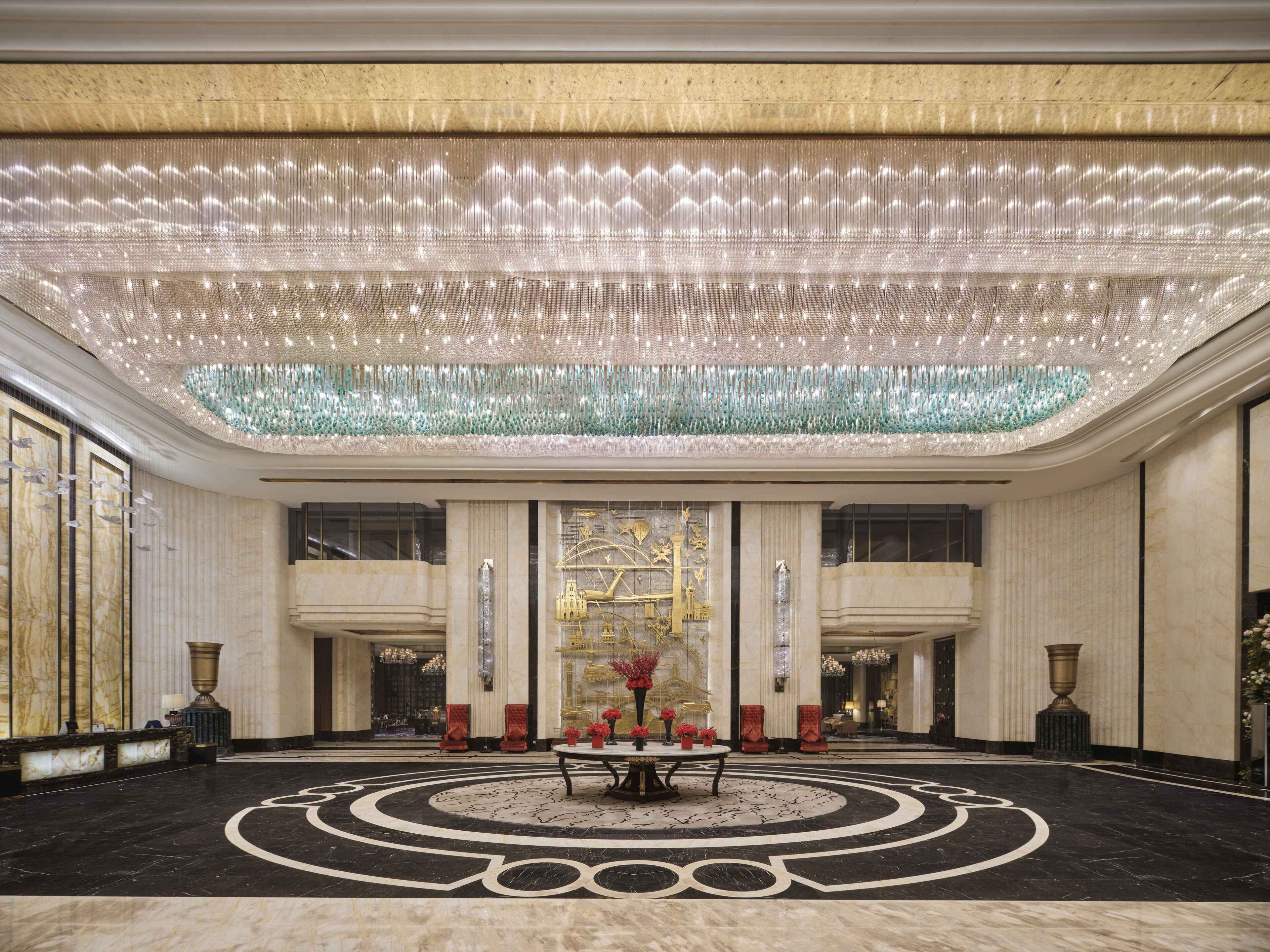 Un hall d’entrée spacieux, agrémenté d’un magnifique lustre, d’un sol en marbre et d’un grand mur décoratif.