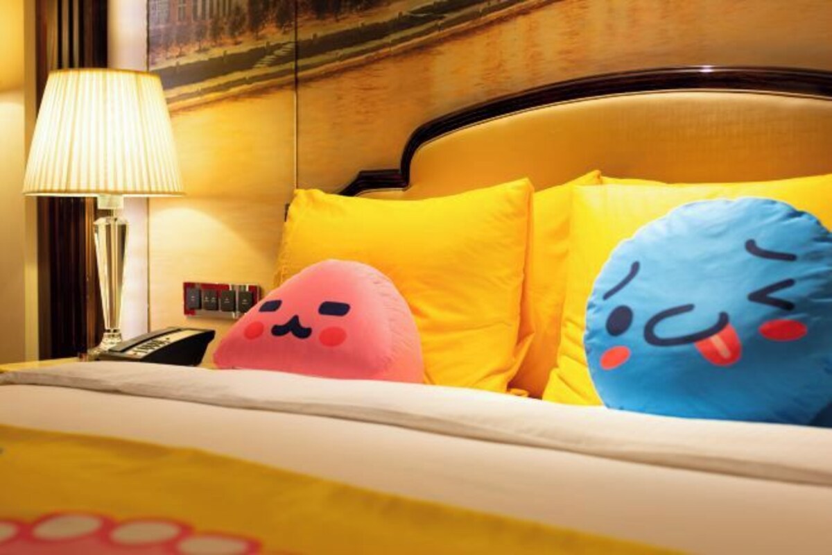 Een hotelkamer met een bed, een lamp en twee kussens met tekenfilmgezichten.