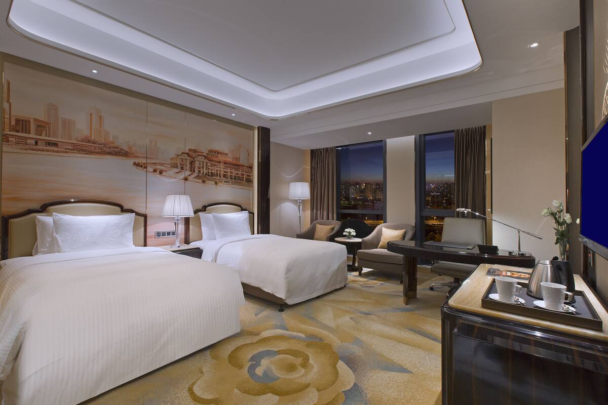 Une chambre d’hôtel avec deux lits, un bureau avec une machine à café, une chaise et un téléviseur.