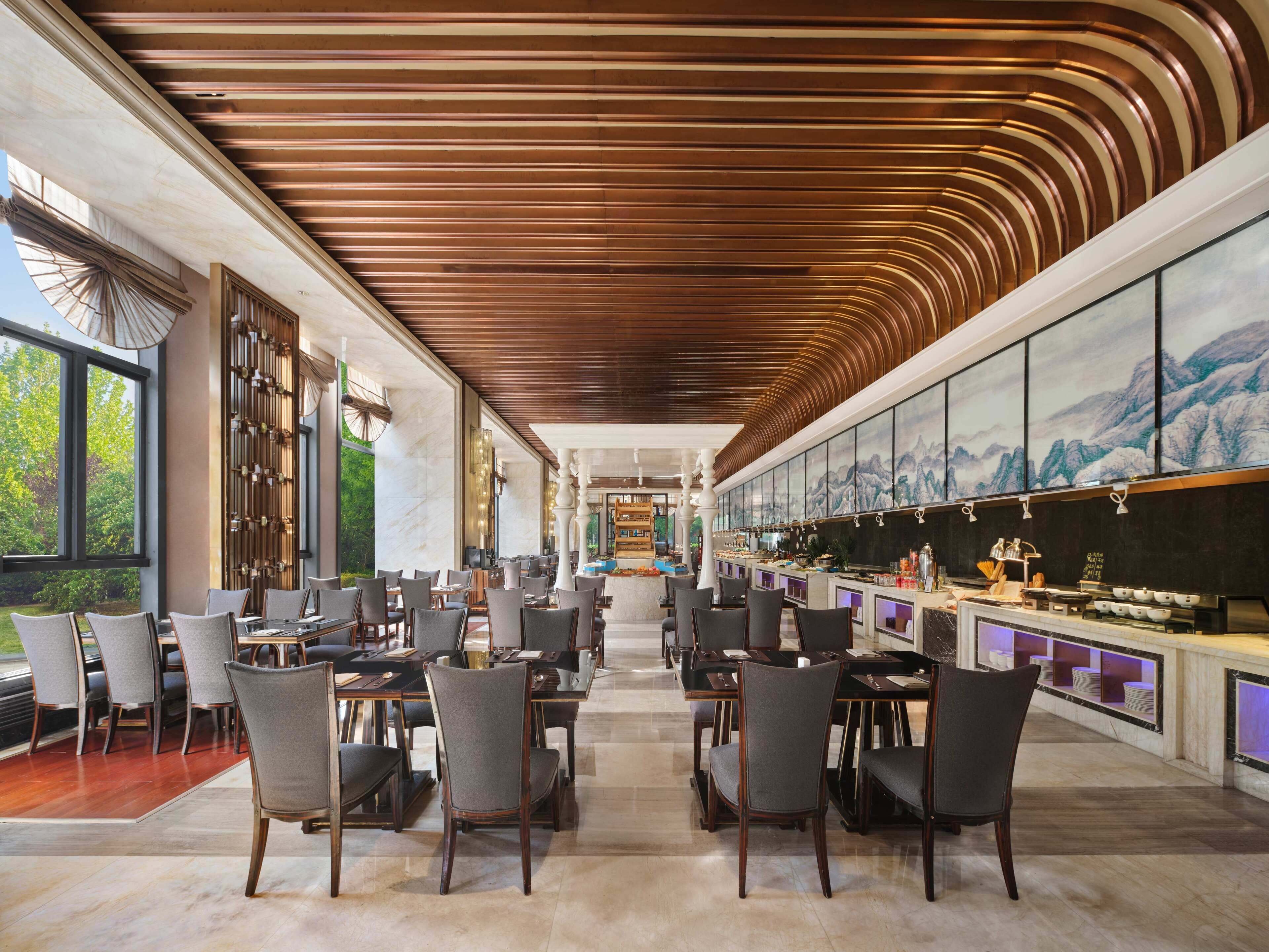 A spacious restaurant with high ceilings and a modern design, featuring multiple dining tables and chairs.