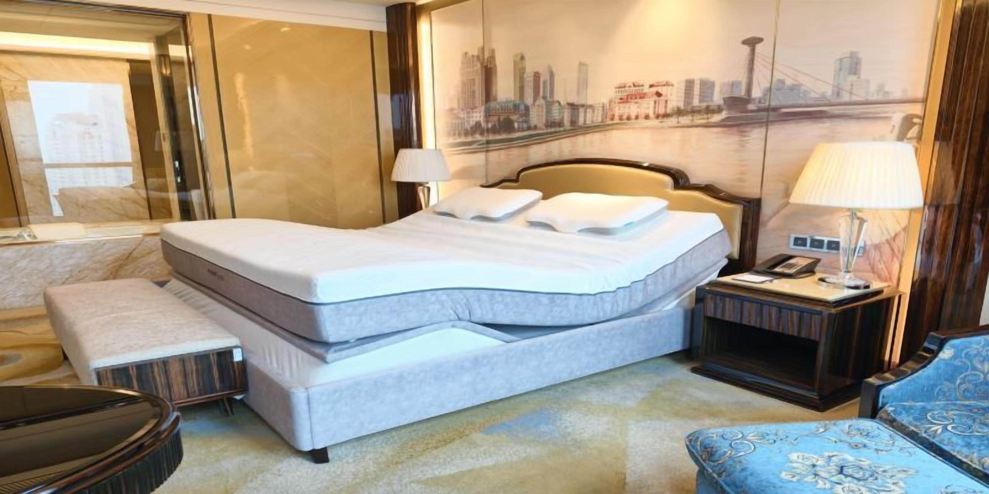 A hotel room with a large bed, a bedside table with a lamp, a small table, and a chair.