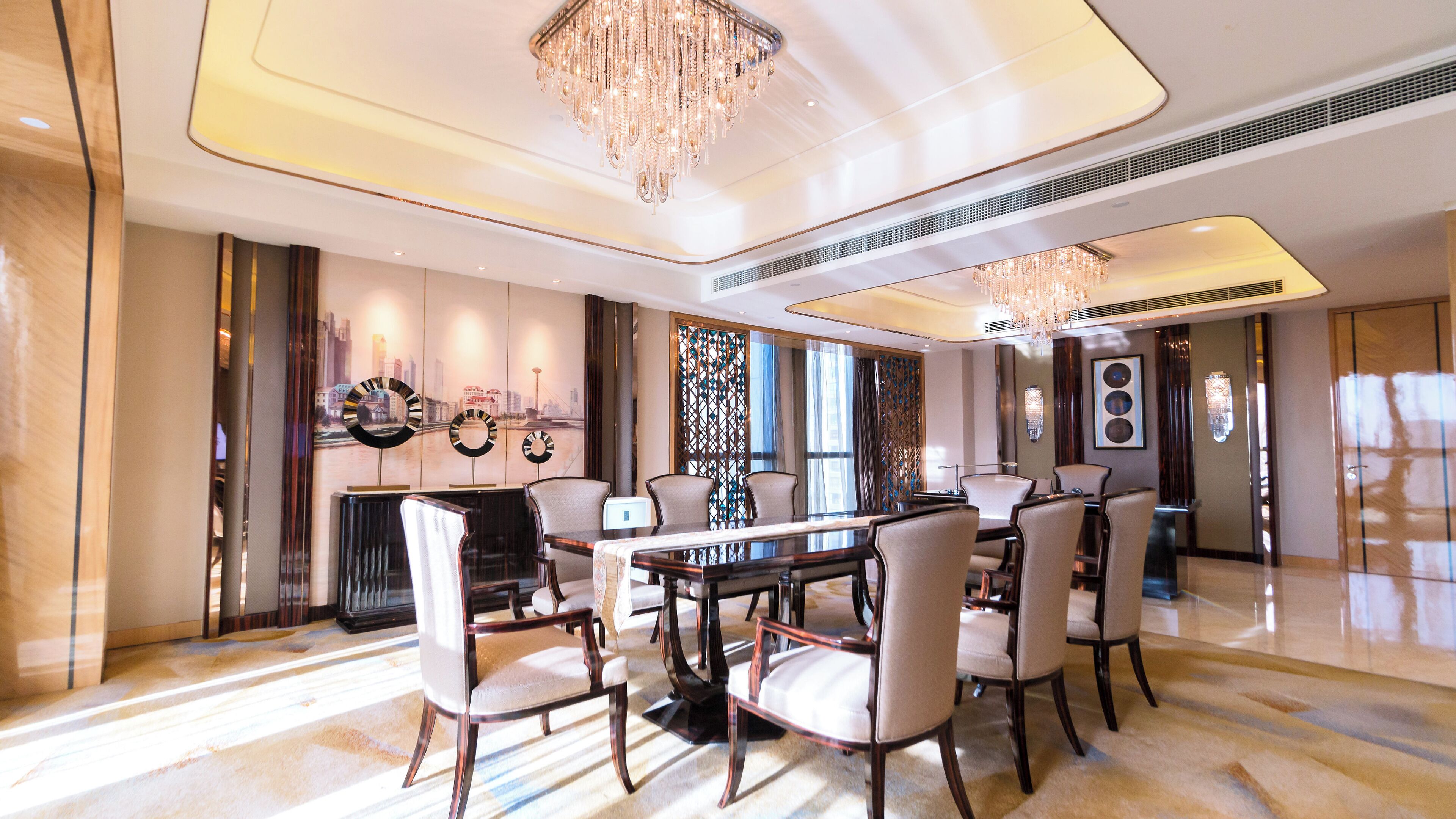 A spacious dining area with a large round table, elegant chairs, and a chandelier.