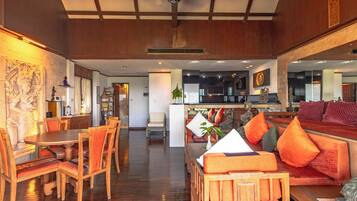 A spacious room with a wooden dining table and chairs, a sofa with orange cushions, and a kitchen area in the background.