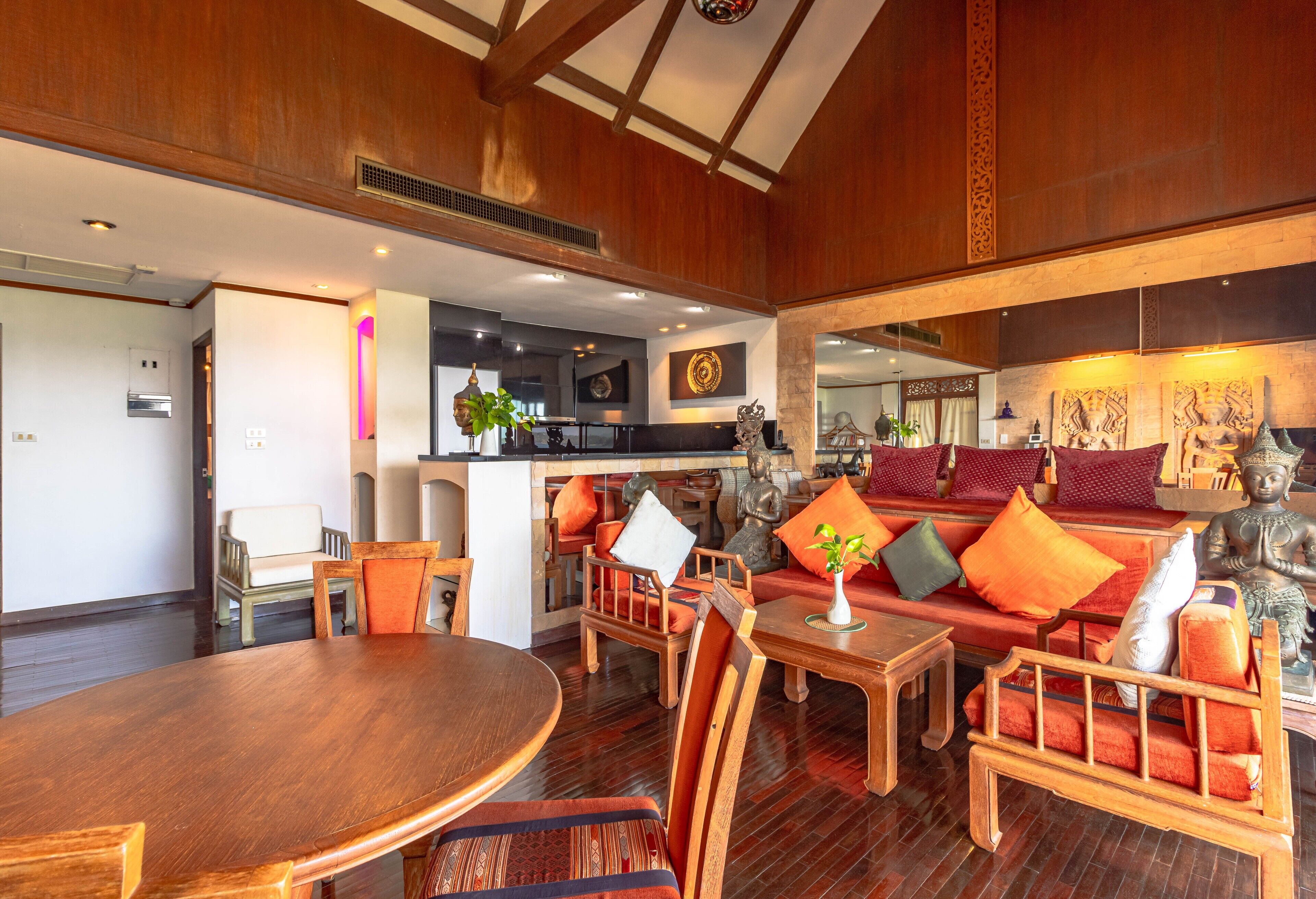 A spacious lobby with a wooden floor, a round dining table, and a sofa with colorful cushions.