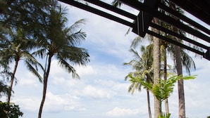 A covered outdoor seating area with wicker chairs and a view of the beach and ocean. - Kamala Beach Estate (Kamala)