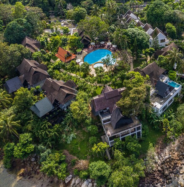 Vista aérea de un resort con varias cabañas, una piscina central y exuberante vegetación que rodea la propiedad.