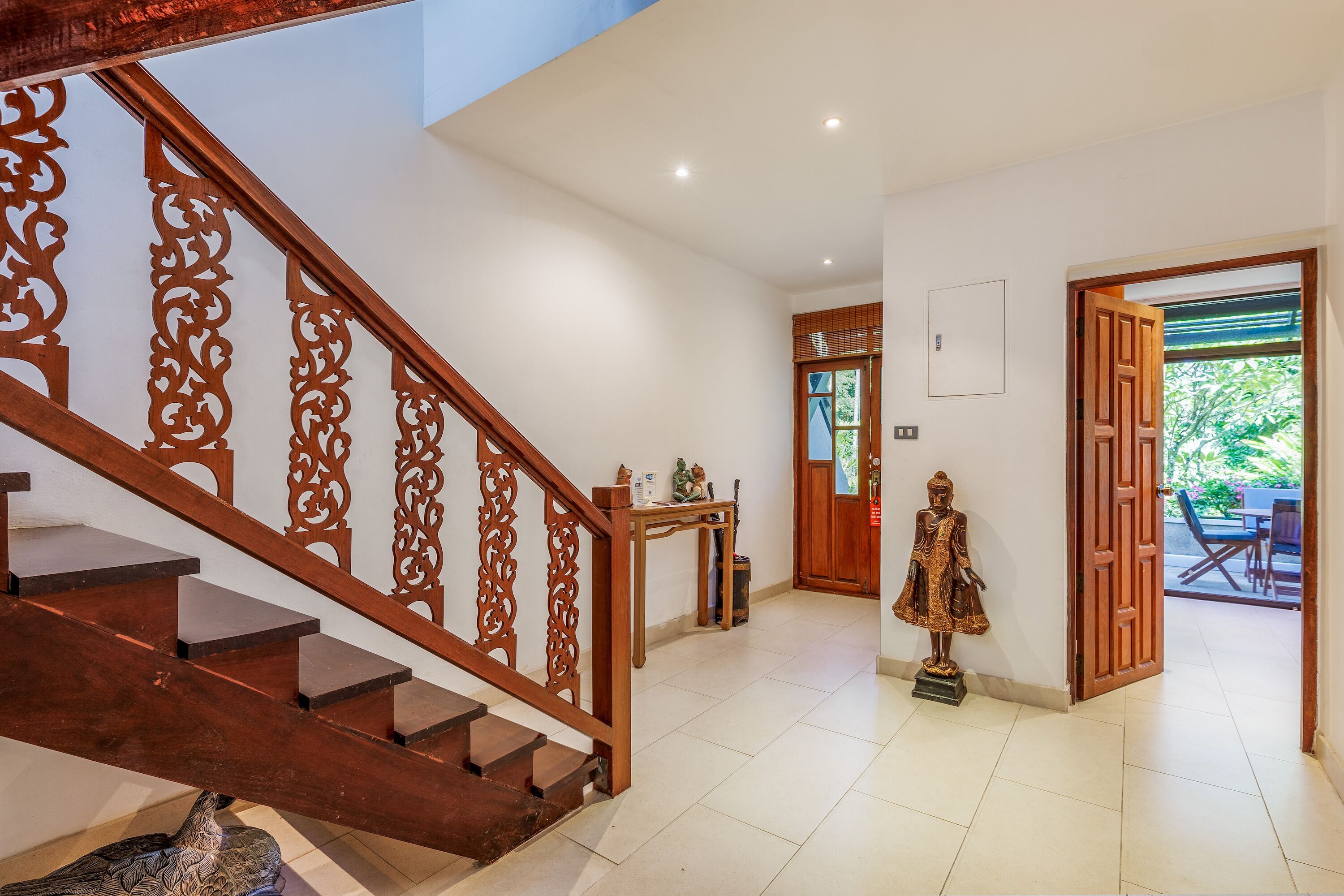Una escalera con barandales de madera ornamentados, una estatua y una puerta que da a un espacio exterior.