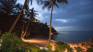 A beach with palm trees, a rocky shoreline, and a building in the background. - Kamala Beach Estate (Kamala)
