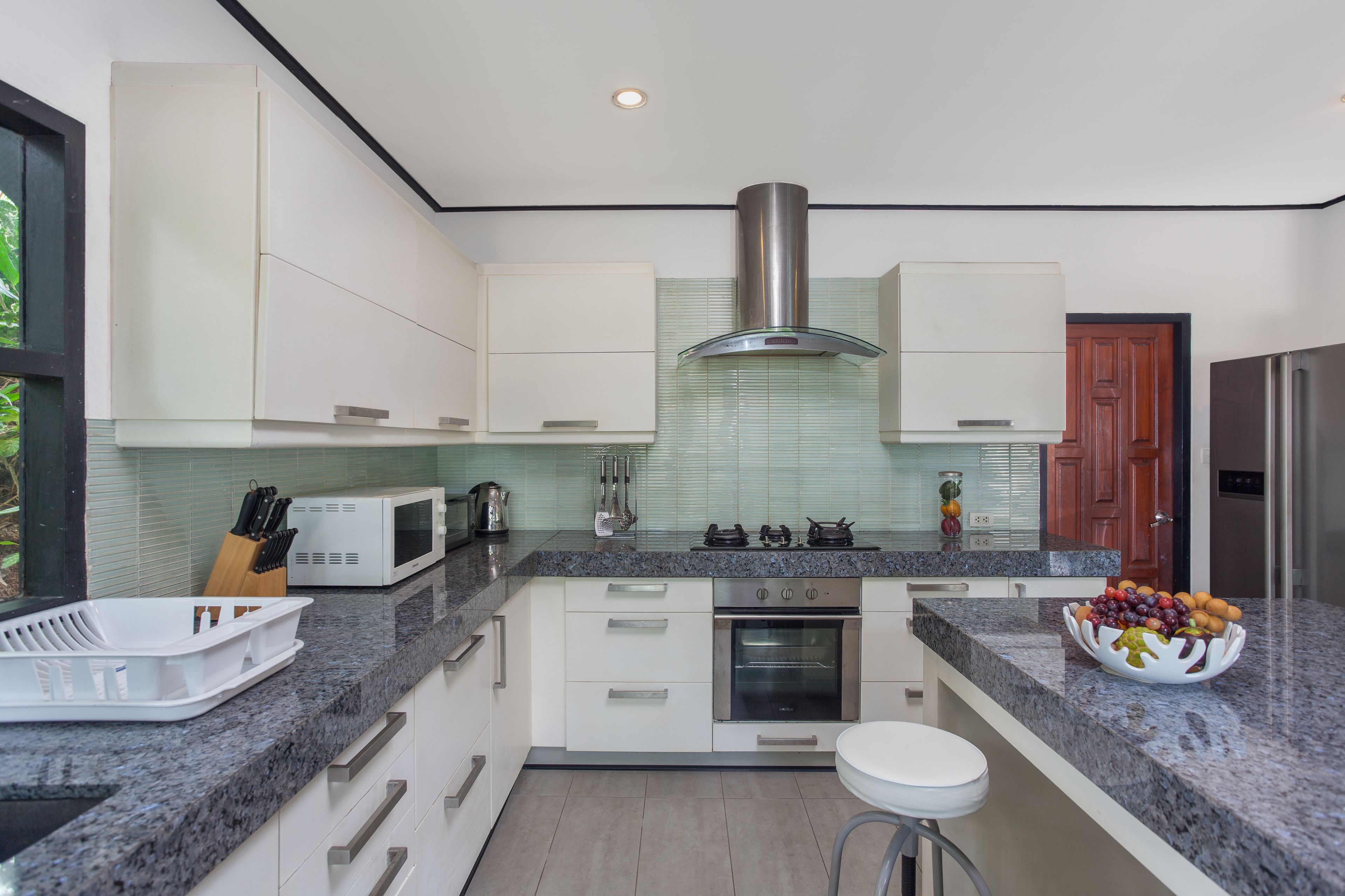 Una cocina moderna con gabinetes blancos, una campana extractora de acero inoxidable, un microondas y un horno empotrado.