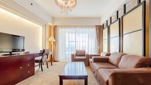 Een moderne hotelkamer met een flatscreen televisie, een houten kast, een bank, een salontafel en een groot raam met gordijnen.