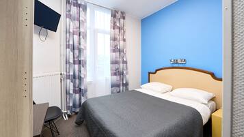 Een hotelkamer met een bed, een bureau, een aan de muur bevestigde televisie en een raam met gordijnen.