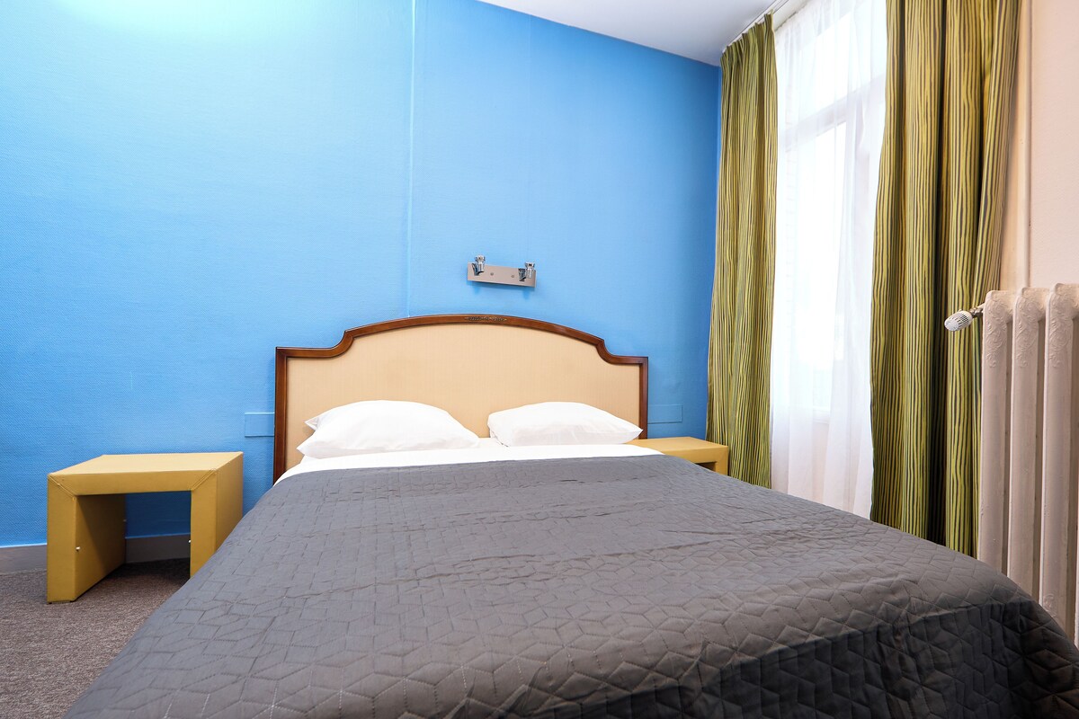A neatly made bed with a quilted cover, a bedside table, and a wall-mounted light fixture.