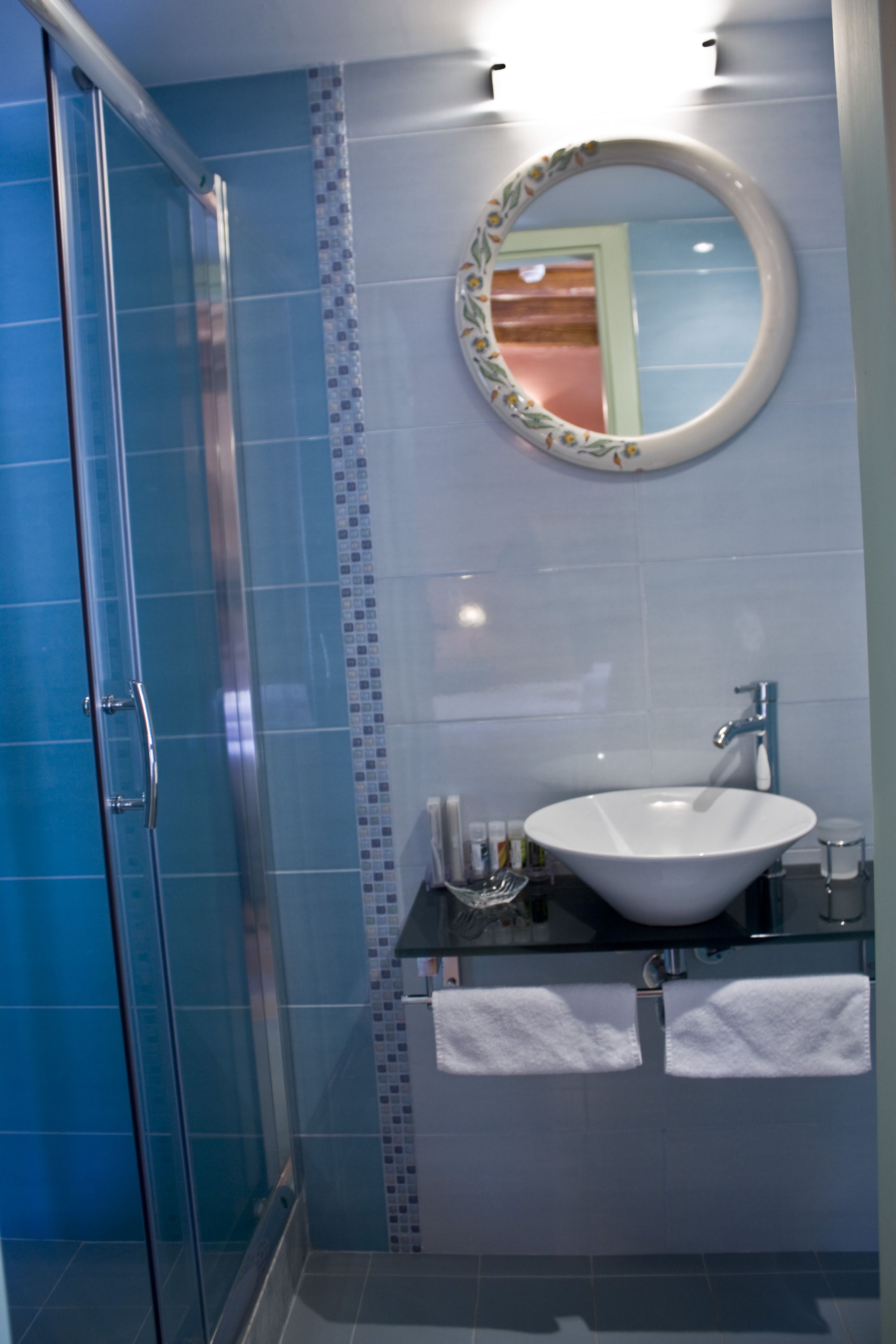 Un baño con cabina de ducha de vidrio, un lavabo blanco y un espejo con marco floral.