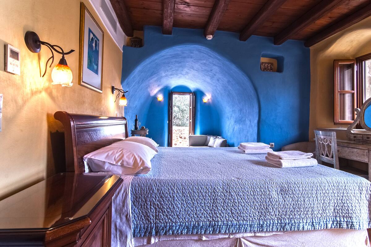 Quarto com cama grande, cabeceira de madeira e teto azul em arco.