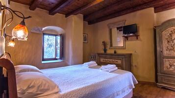 A bedroom with a wooden ceiling, a bed with white linens, a window, a TV on a shelf, and a wooden wardrobe.