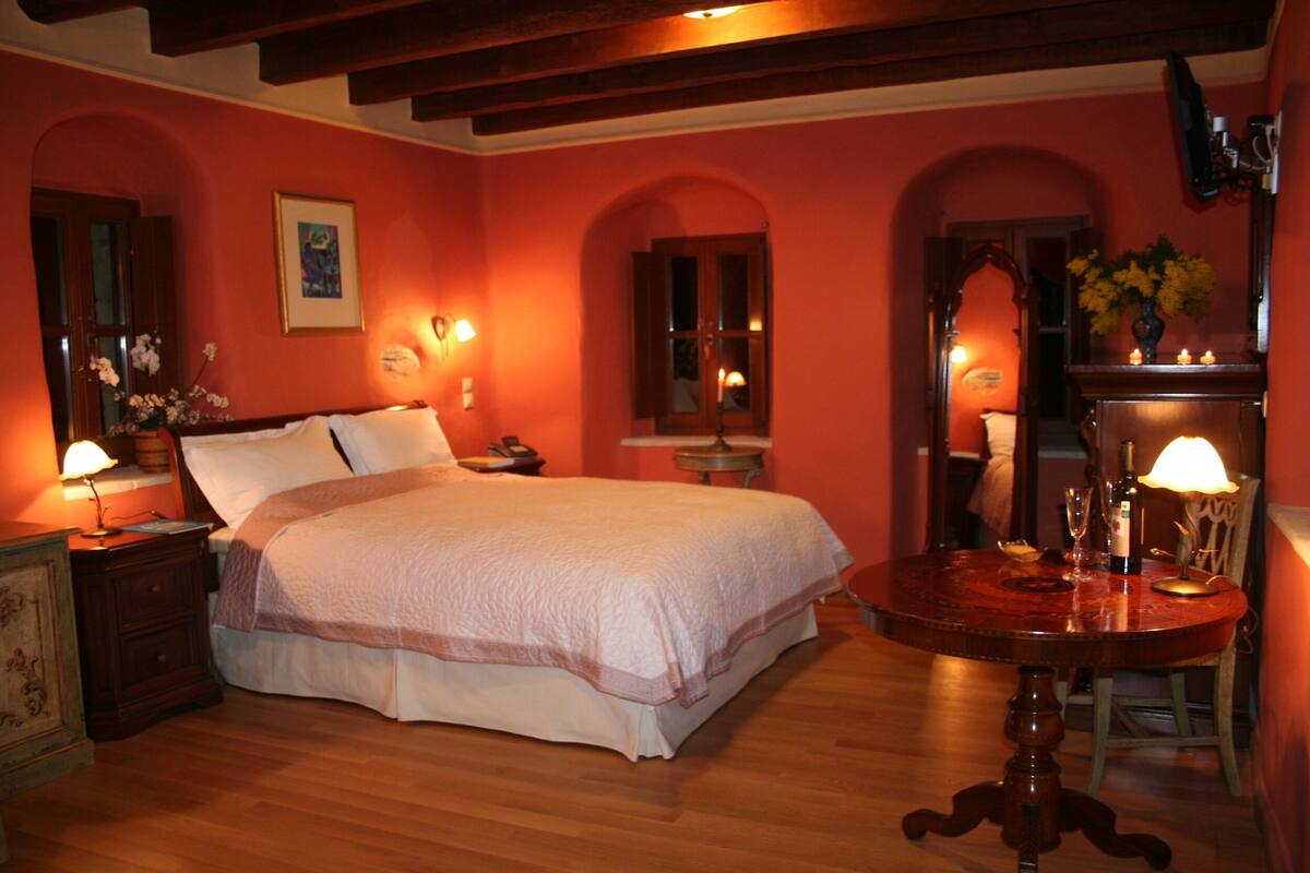 Quarto com cama, mesa de cabeceira, abajur e uma mesa redonda com cadeira.