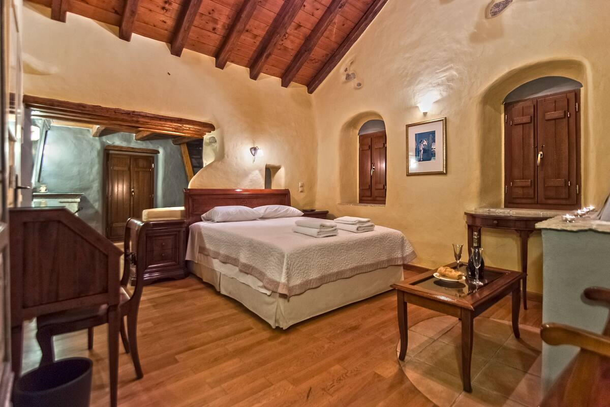 Quarto com cama de madeira, mesa de cabeceira com abajur, cadeira e escrivaninha de madeira com cadeira.
