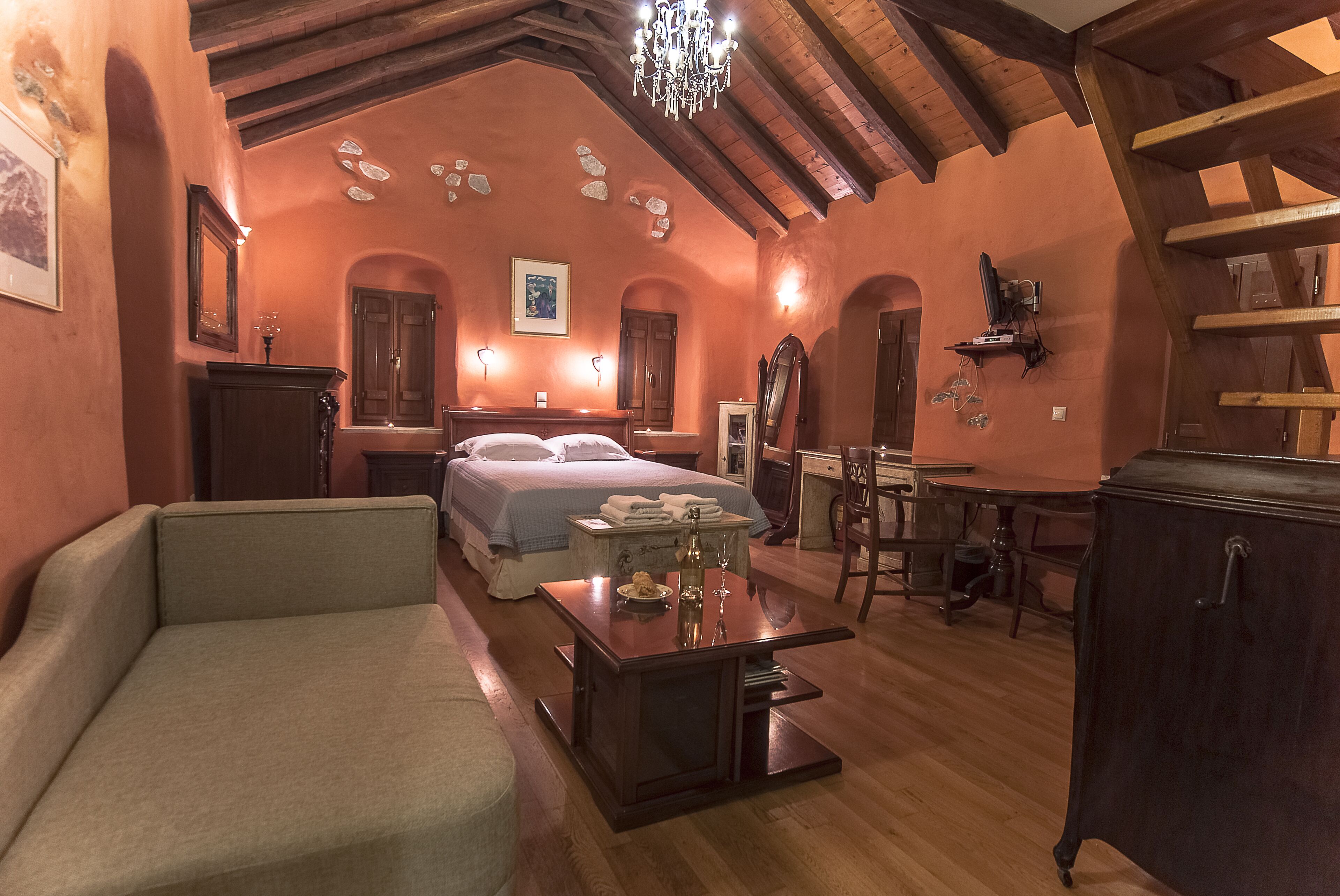 Una habitación acogedora con cama, sofá, mesa con un florero y copas de vino, y techo de madera.