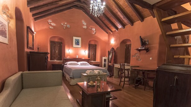 A cozy room with a bed, a sofa, a table with a vase and wine glasses, and a wooden ceiling.