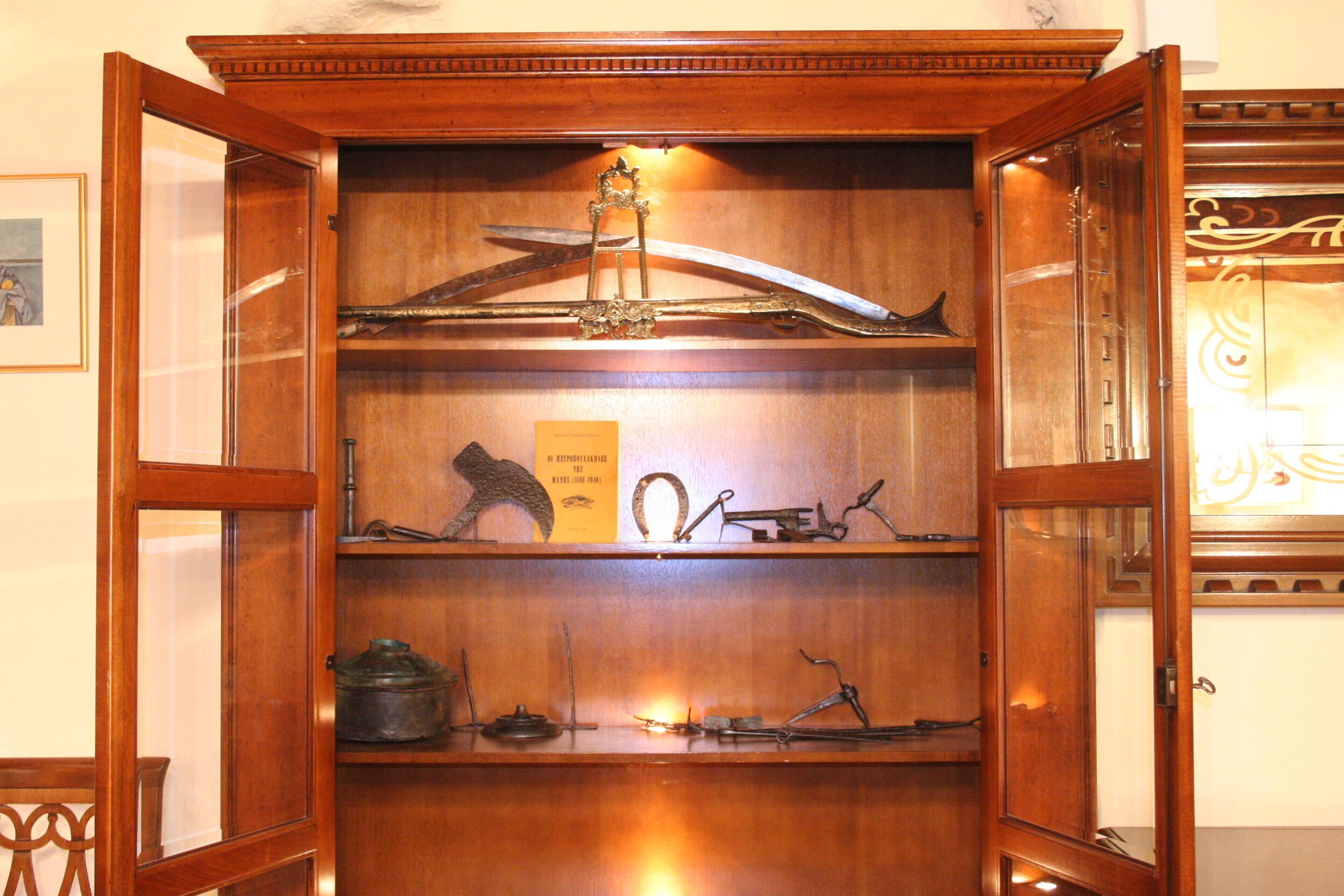 A wooden display cabinet with glass doors, containing various antique items such as a sword, a book, and other historical artifacts.