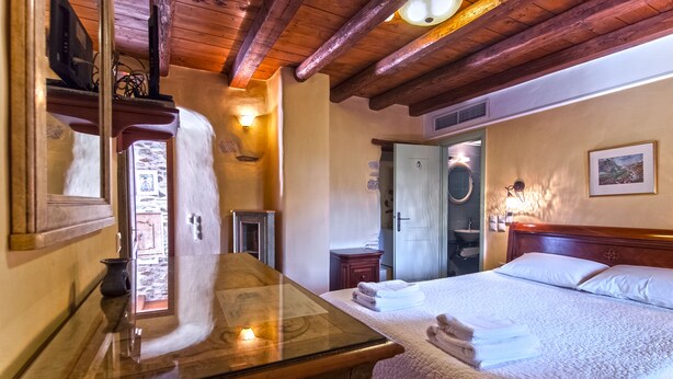 Een knus hotelkamer met een houten plafond, een groot bed met witte lakens, een nachtkastje en een spiegel.