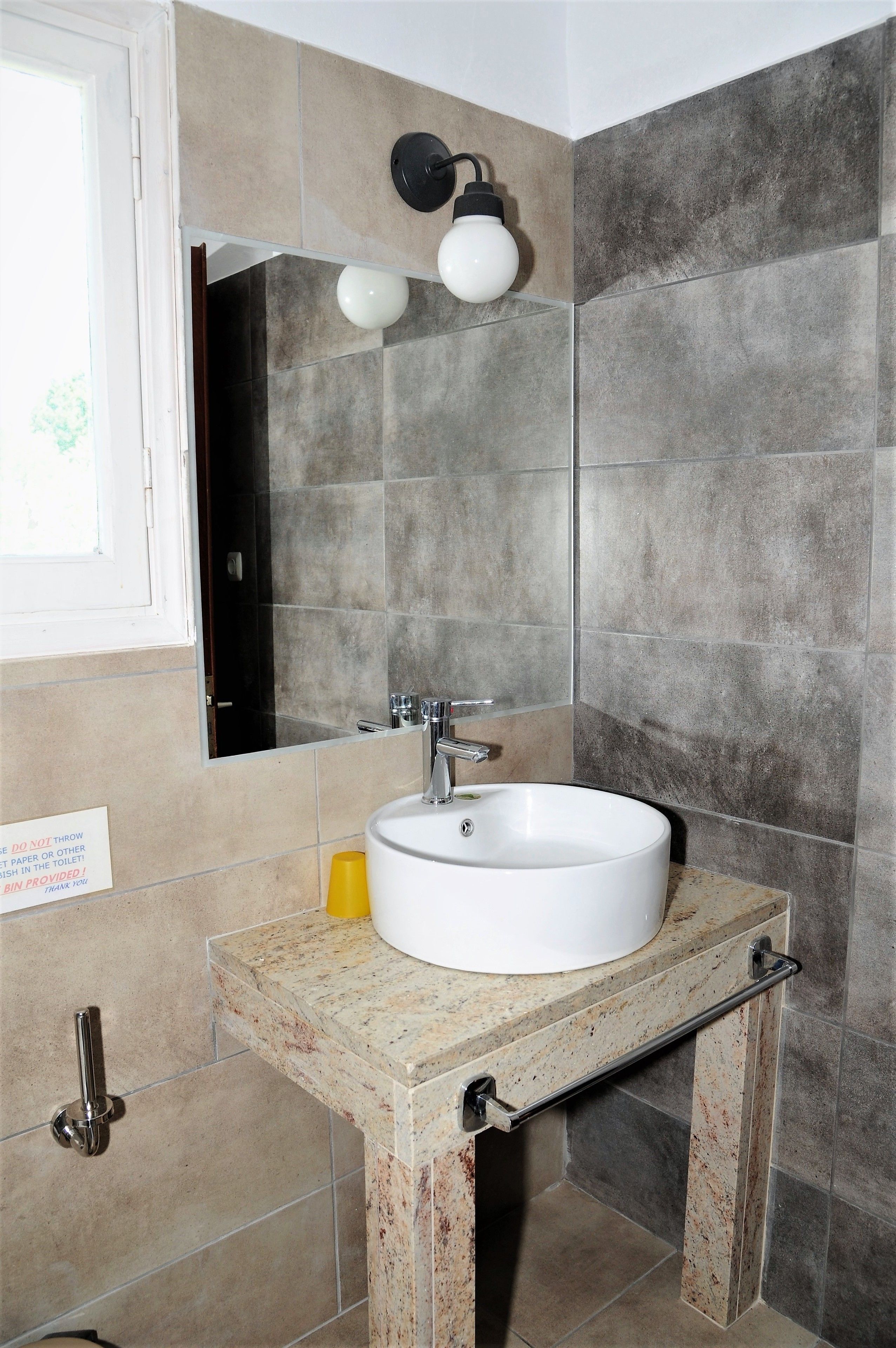 Un baño con un lavamanos blanco, un espejo y una lámpara fijada a la pared.