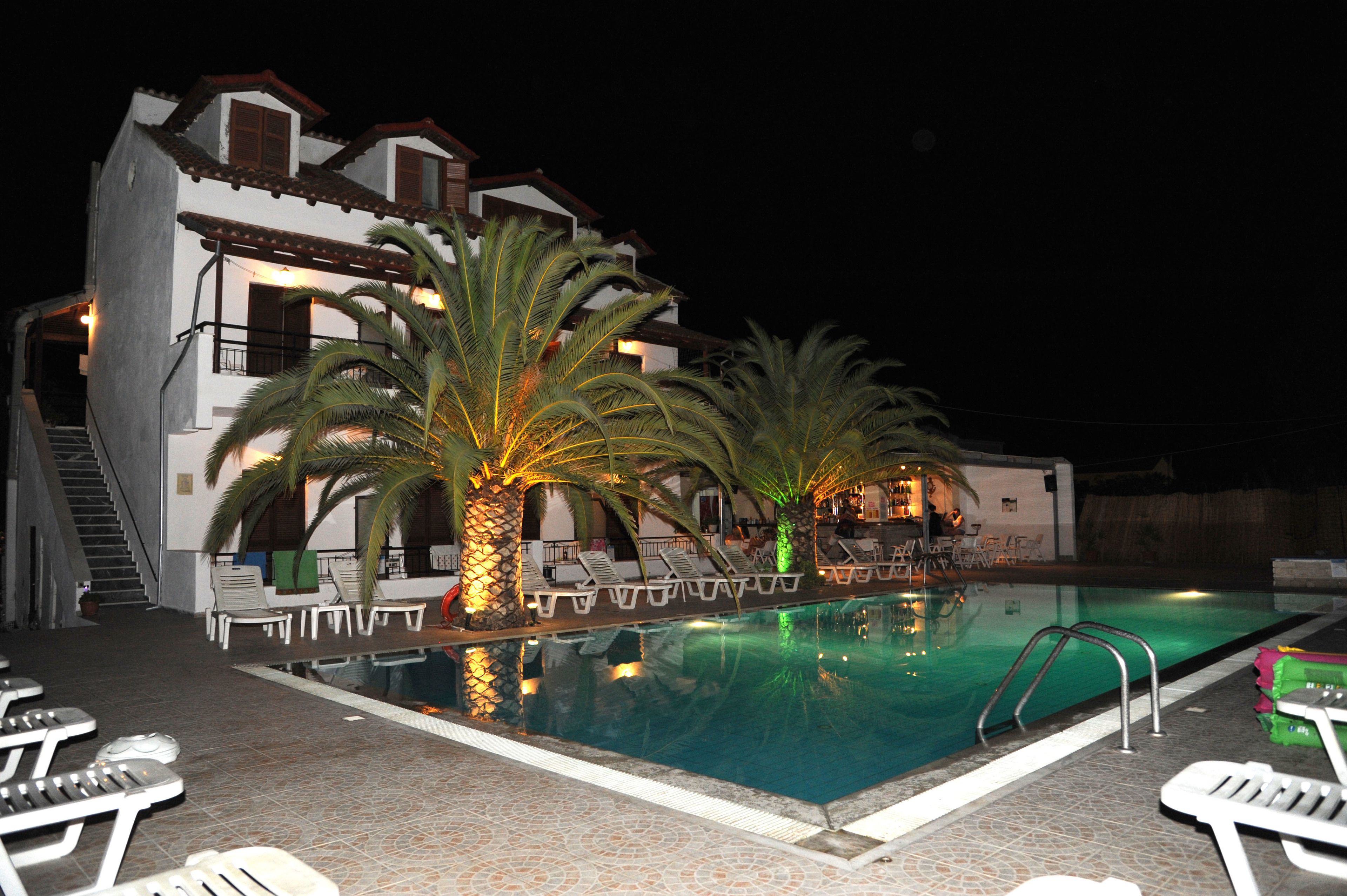 A swimming pool with lounge chairs and palm trees, surrounded by a building with multiple balconies.