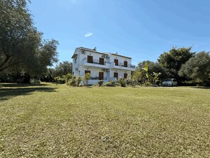 Un edificio de dos pisos con balcón, rodeado de césped cuidado y árboles.
