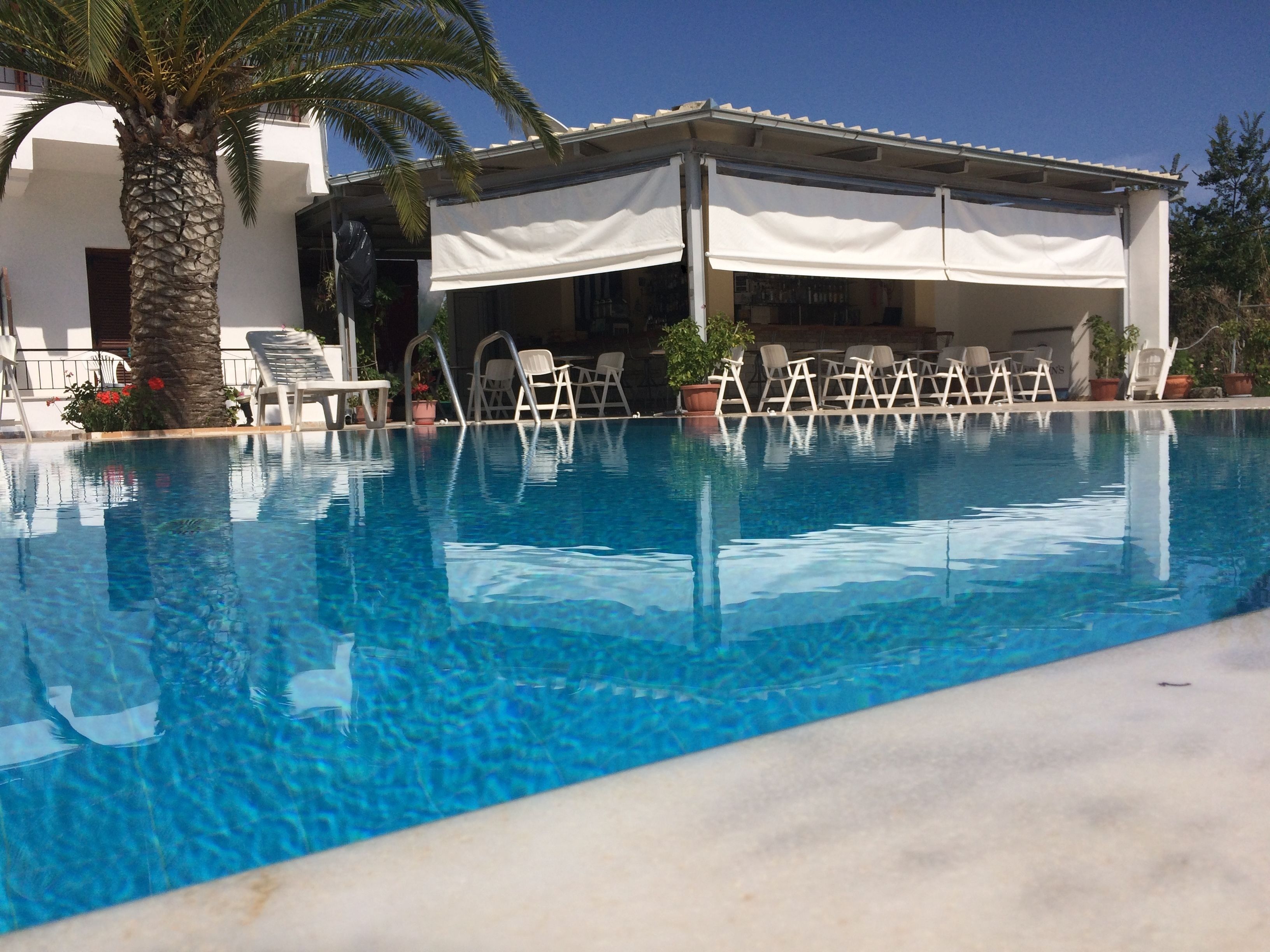 Una piscina con agua cristalina azul, rodeada de sillones blancos y un área de estar techada.