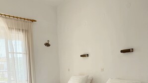 A room with two beds, a window with curtains, and a wall-mounted light fixture.