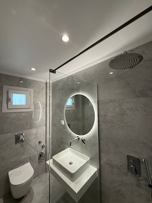 Ein modernes Badezimmer mit einer Glaskabine zur Dusche, einem freistehenden Waschbecken und einem großen Spiegel.
