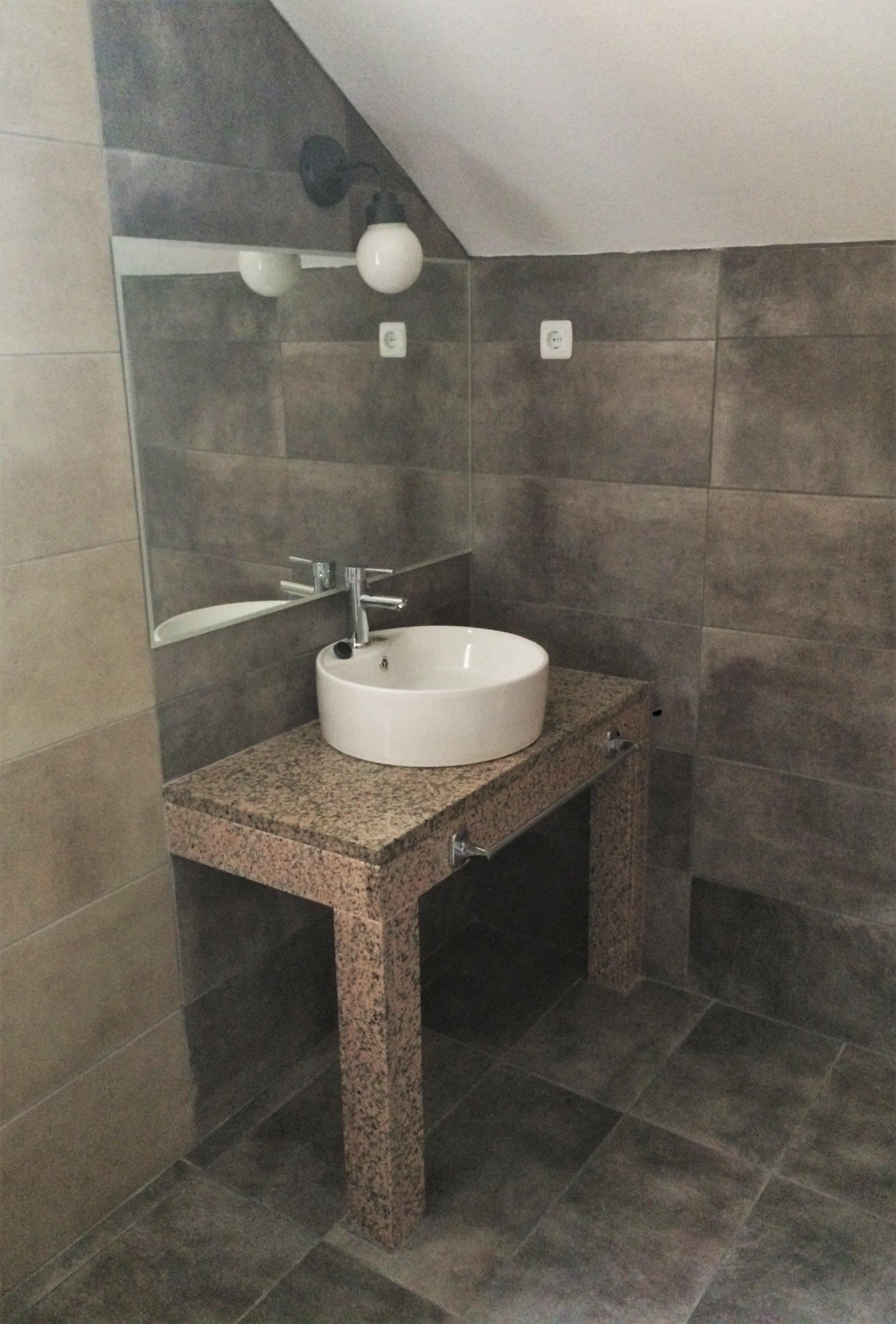Ein Badezimmer mit einem weißen Waschbecken, einer Granit-Arbeitsfläche und dunkel gefliesten Wänden.