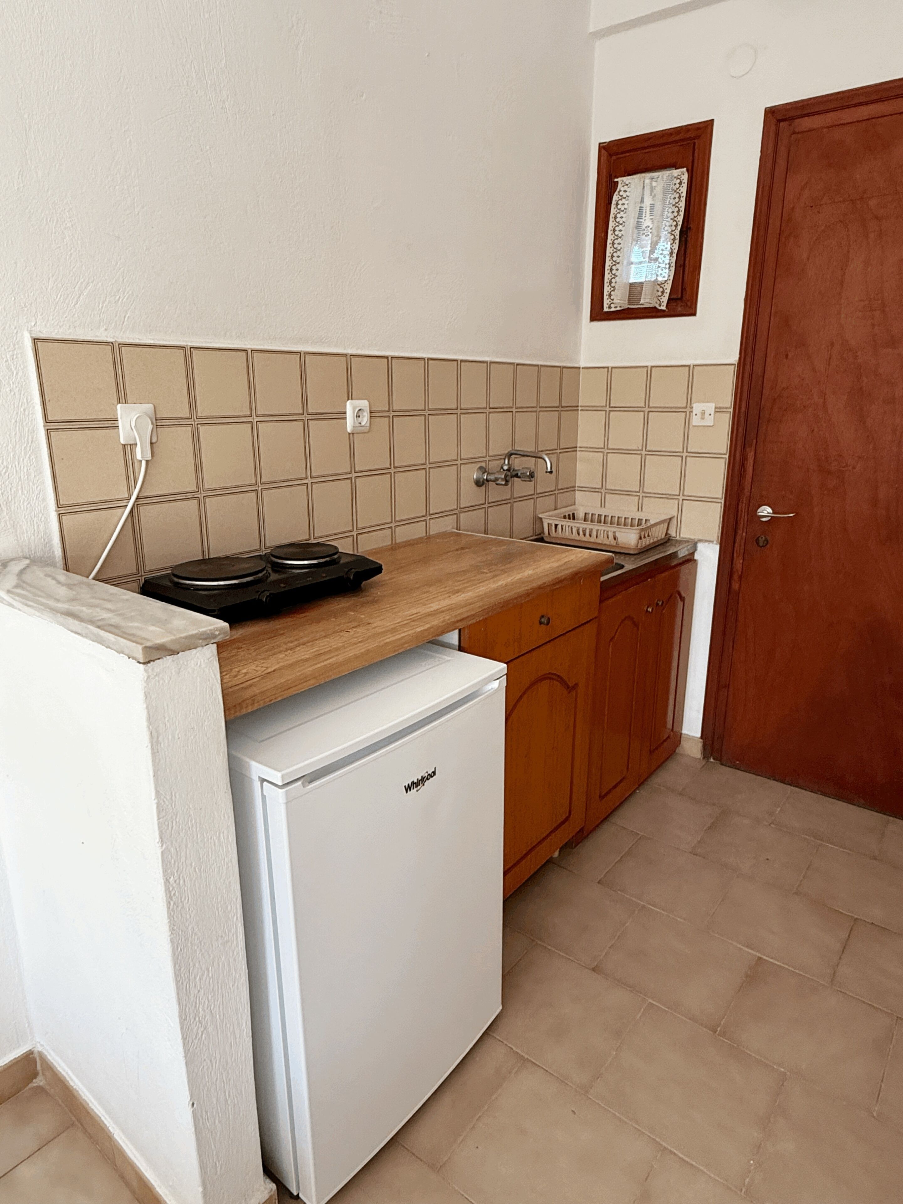 Una cocina compacta con refrigerador, lavamanos y encimera de madera.