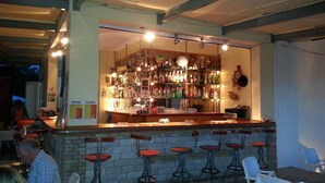 A bar area with a brick counter, multiple stools, and shelves stocked with bottles.