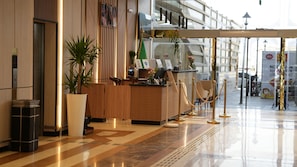 A hotel reception area with a reception desk, a potted plant, and a seating area.