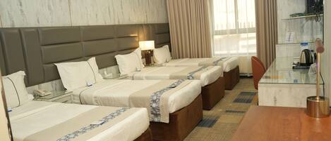 A hotel room with four beds, a desk, a telephone, and a lamp.