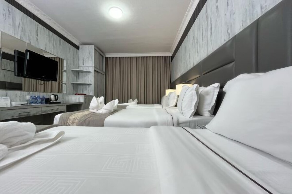 A hotel room with two beds, a flat-screen TV, a minibar, and a large mirror.