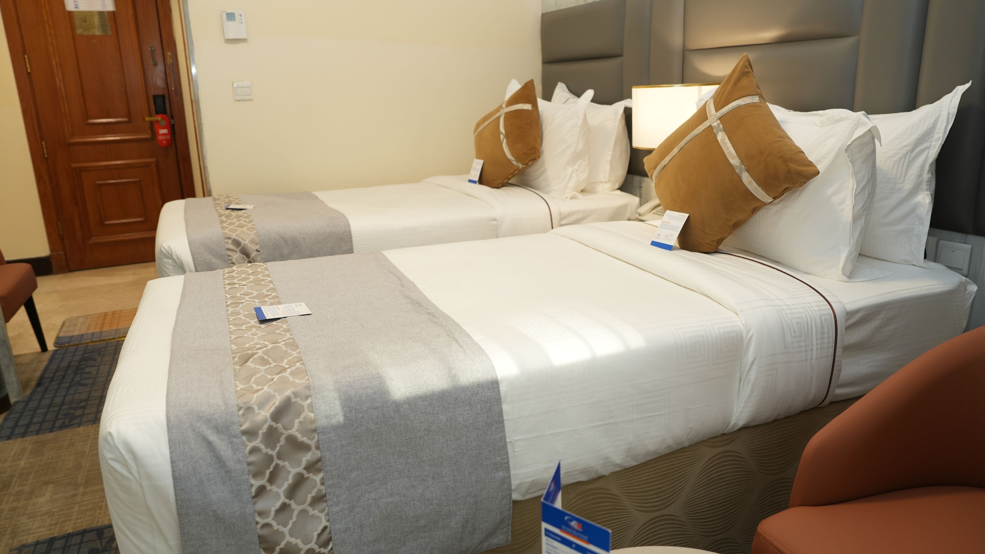 Hotellihuone, jossa on kaksi sänkyä, yöpöytä, lamppu ja tuoli.