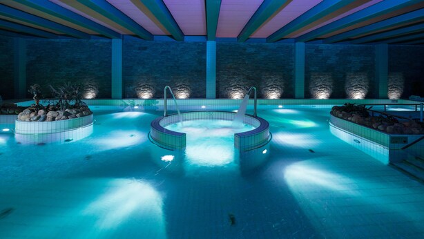 Una gran piscina interior amb diverses banyeres d'hidromassatge, envoltada de parets de pedra i un paviment de rajola.