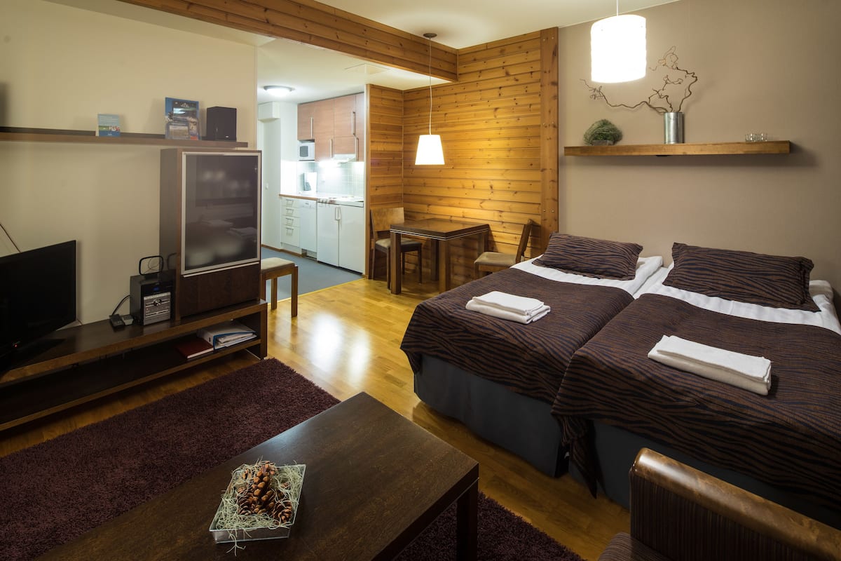 A hotel room with a wooden interior, a flat-screen TV, a desk with a computer, and a bed with two pillows.