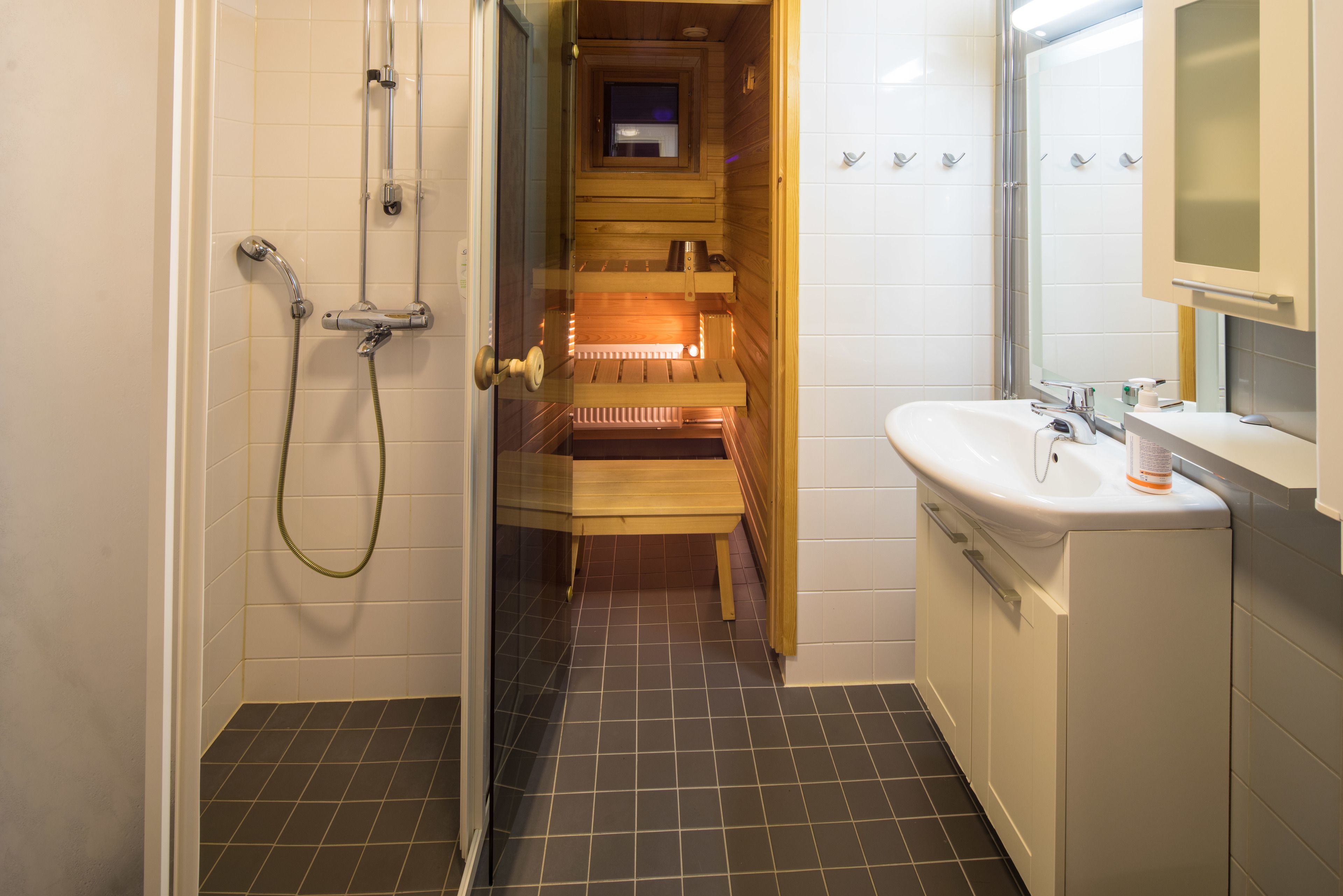 Un baño con ducha, un banco de madera, un lavamanos y un espejo.